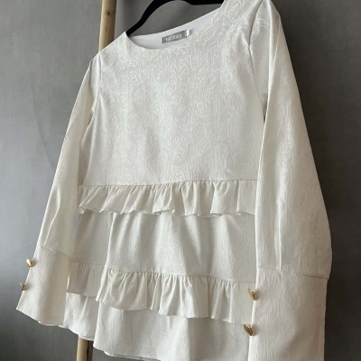 Blusa branca texturizada com folhos e botões dourados nas mangas pendurada