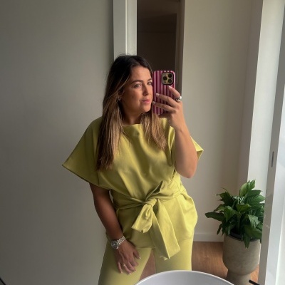 Mulher com conjunto amarelo e telemóvel com capa rosa às riscas na mão