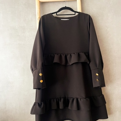 Vestido castanho escuro com folhos e botões dourados pendurado numa escada de madeira