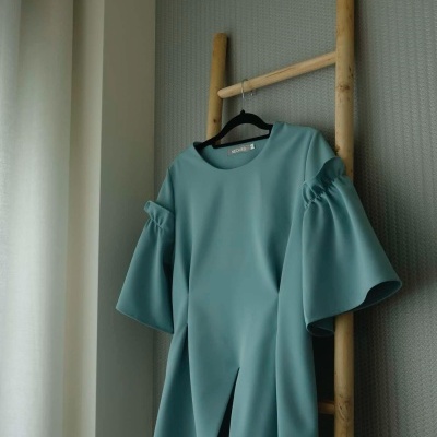 Vestido azul esverdeado com mangas volumosas pendurado numa estrutura de madeira