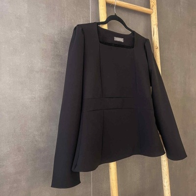 Blazer preto feminino pendurado numa escada de madeira contra parede cinzenta