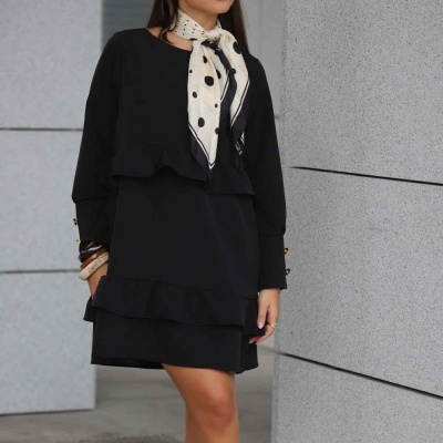 Mulher com vestido preto e lenço de bolinhas em ambiente urbano