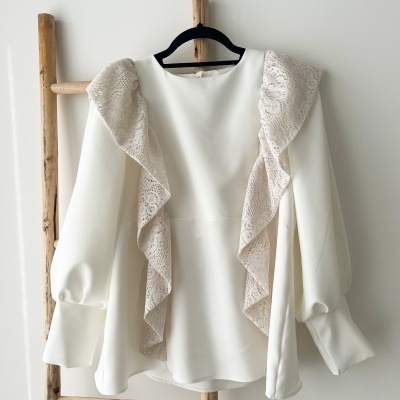 Blusa branca com folhos de renda bege pendurada num cabide preto