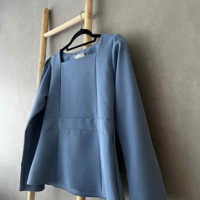 Blusa azul céu com mangas compridas pendurada num cabide preto numa estrutura de madeira