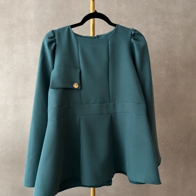 Blusa verde água com manga longa e volume nos ombros pendurada num cabide