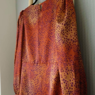 Vestido com padrão de manchas vermelho e laranja pendurado num cabide preto