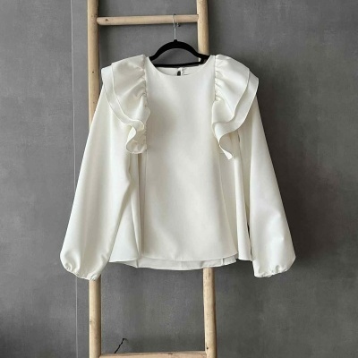 Blusa branca com folhos pendurada numa escada de madeira