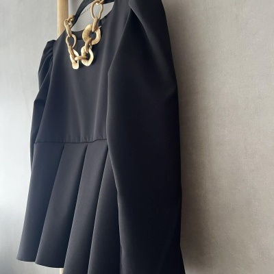 Vestido preto curto com saia pregueada e colar dourado pendurado em cabide de veludo