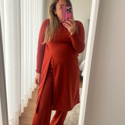 Mulher usando túnica e calças castanhas avermelhadas diante de espelho