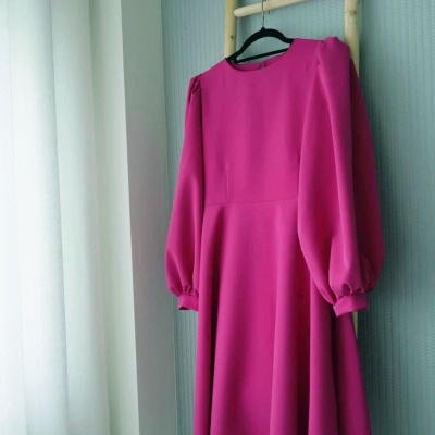 Vestido rosa pendurado numa escada de madeira junto a uma parede azul e cortina branca