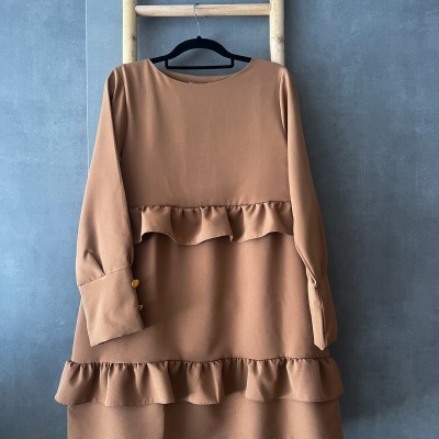 Vestido castanho claro com folhos pendurado numa escada de madeira