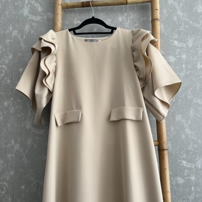 Vestido bege claro com folhos nas mangas pendurado em cabide preto numa escada de bambu