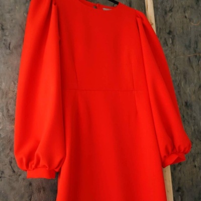 Vestido laranja com mangas bufantes pendurado numa estrutura de madeira