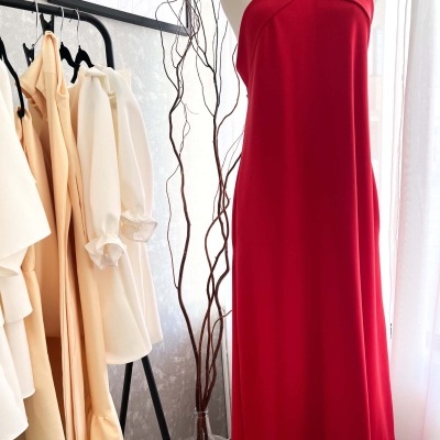 Vestido vermelho em manequim ao lado de vestidos creme em cabideiro preto