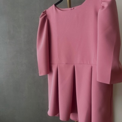 Vestido rosa de manga comprida com ombros franzidos e saia com pregas pendurado em cabide preto