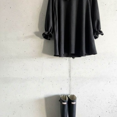 Vestido preto com folhos e botas pretas junto a parede branca