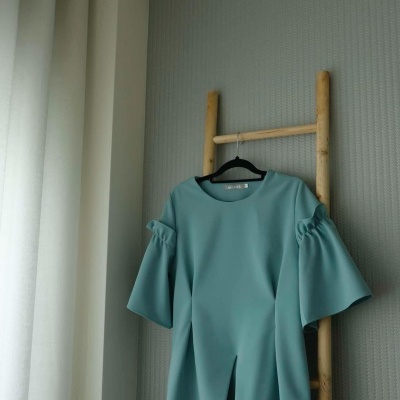 Vestido azul claro pendurado numa escada de bambu junto a uma parede cinzenta