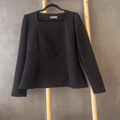 casaco preto liso com gola quadrada pendurado numa escada de madeira