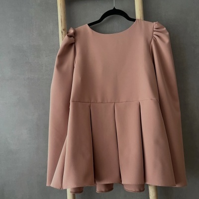 Vestido rosa claro de manga comprida com pregas e ombros franzidos pendurado numa cabide preta