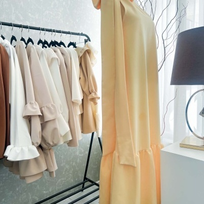 Vestido amarelo com laço no ombro esquerdo exposto em manequim ao lado de roupas claras num cabideiro preto