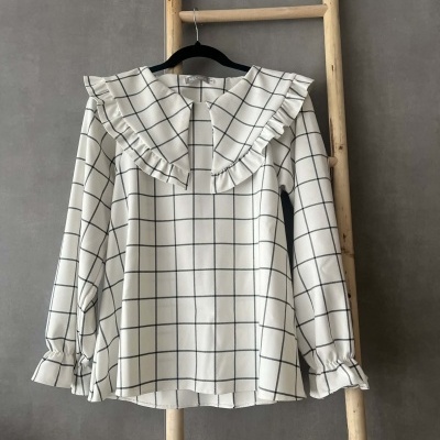 Blusa branca com padrão de grade preta e gola com folhos no cabide