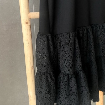 Vestido preto com renda pendurado numa estrutura de madeira.