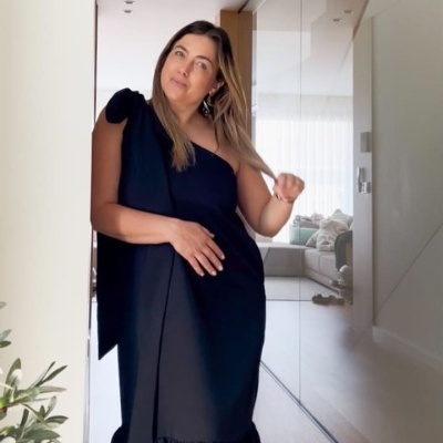 Mulher a usar vestido preto longo num ambiente interior com chão de madeira.