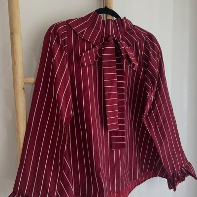 Blusa vermelha riscada com folhos, laço e punhos folhados pendurada numa escada de madeira.