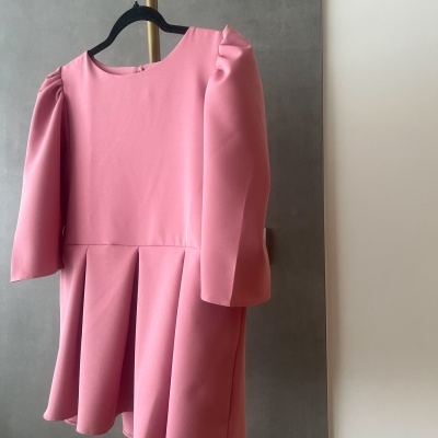 Vestido cor-de-rosa com mangas bufantes e saia plissada num cabide preto