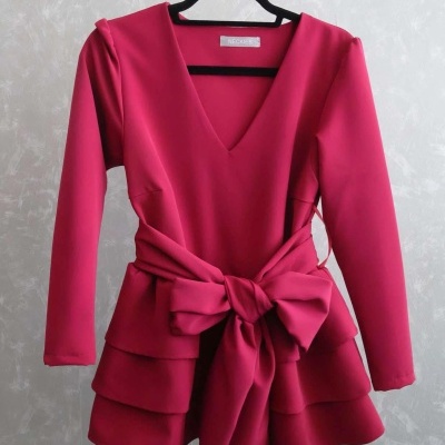 Blusa rosa com laço e mangas compridas pendurada num cabide preto