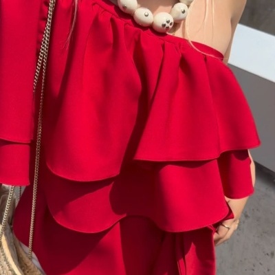 Blusa vermelha com folhos, colar de contas bege e bolsa de palha.