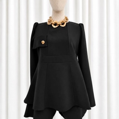 Fato feminino preto com saia assimétrica, manga comprida, bolso com botão dourado e colar dourado em manequim frente a cortinas brancas