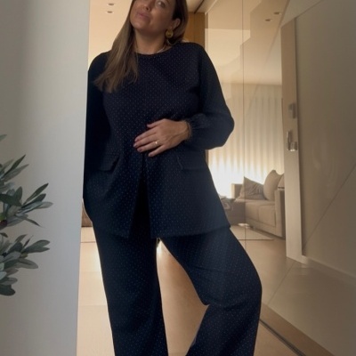 Conjunto de roupa preta com pontos brancos, casaco e calças, em ambiente interior claro com planta e sofá ao fundo