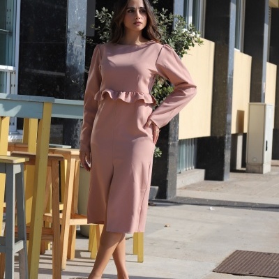 Mulher vestindo vestido rosa claro com folho na cintura e sapatos creme em ambiente urbano