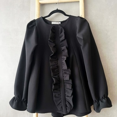 Blusa preta com folhos pendurada numa escada de madeira