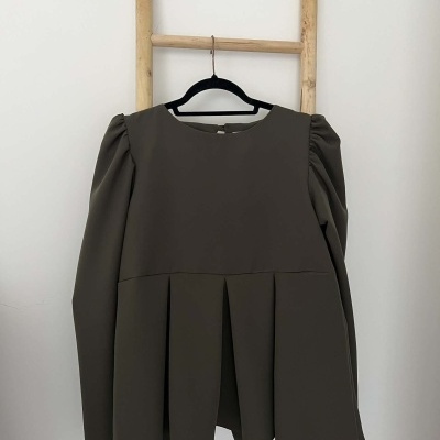 Blusa castanha escura com mangas longas franzidas pendurada numa escada de madeira.