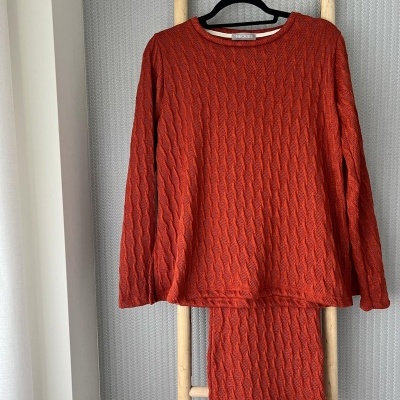 Conjunto de roupa de malha laranja pendurado em cabide numa estrutura de madeira