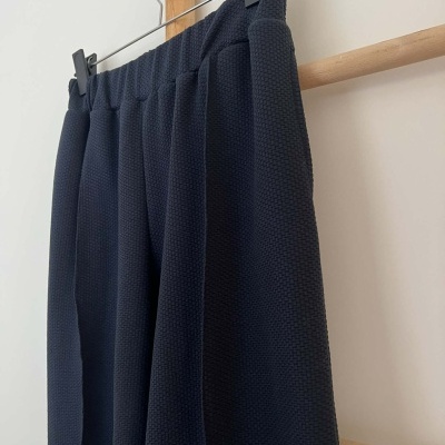 Calças azuis escuras texturadas penduradas com cabide num suporte de madeira