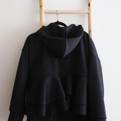 Casaco preto com capuz pendurado numa escada de madeira clara