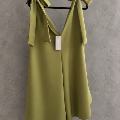 Vestido verde-oliva com alças de laço pendurado num cabide preto.