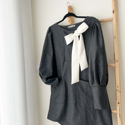 Vestido cinzento escuro com laço branco pendurado numa escada de madeira