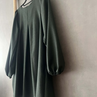 Vestido verde escuro com mangas compridas arfadas pendurado numa estrutura de madeira.