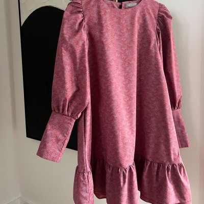 Vestido rosa com padrão floral e mangas bufantes pendurado em cabide.