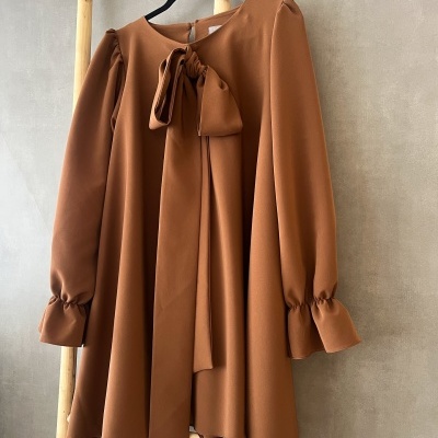 Vestido castanho com laço frontal e mangas compridas pendurado num cabide