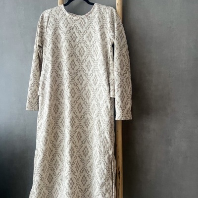 Vestido comprido bege com padrão em relevo pendurado numa escada de madeira