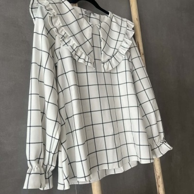 Blusa branca com padrão de quadrícula preta e gola com babados pendurada numa escada