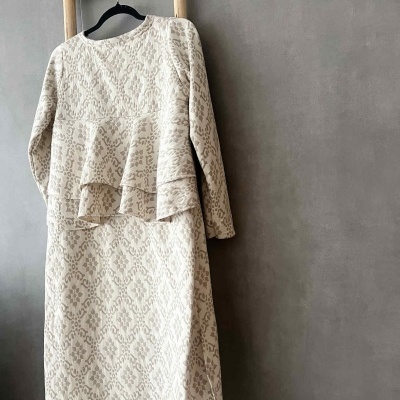 Vestido comprido bege com padrão texturado pendurado num cabide numa escada de madeira