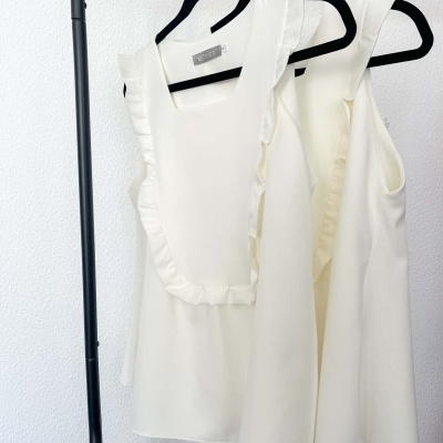 Dois tops brancos em cabides pretos com babados e decote quadrado, em fundo branco