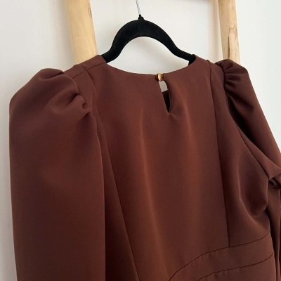 Vestido castanho de manga longa com mangas franzidas pendurado num cabide preto