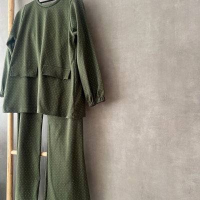 Conjunto de camisola e calças verde-oliva com pontos brancos pendurado em cabide numa estrutura de madeira